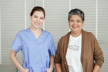Senior asian woman and young asian female physiotherapist standing indoors smiling together in relaxed posture after completing physical rehabilitation program for elderly healthcare support