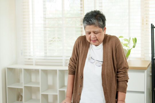 asian senior woman slowly placing hand on lower back while experiencing discomfort during physical therapy session in home clinic designed for elderly rehabilitation and spinal treatment support - Powered by Adobe