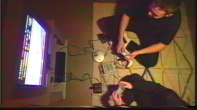 Two boys playing a game late at night on an old school console on a CRT TV with a portable CD player on the floor. View from above