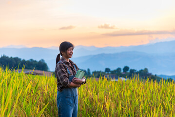 Young Asian woman farmer standing with digital tablet looking into future of agriculture at sunset.