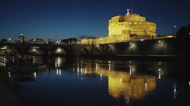 Cinematic shot of bridge and Castel Sant'Angelo at night with mirror reflection on Tiber River water in Rome, Italy. Built by Hadrian emperor as mausoleum in 123AD ancient Roman Empire landmark.