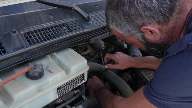 Man tightening a hose clamp in a dirty diesel engine compartment with a green screwdriver