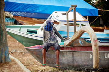 Bali, Indonesia, November 18, 2015. Man sitting on edge of wooden fishing boat outdoors, wearing...