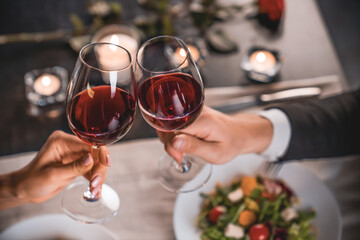 Close up of young couple toasting with glasses of red wine at restaurant. Cropped image of wine...