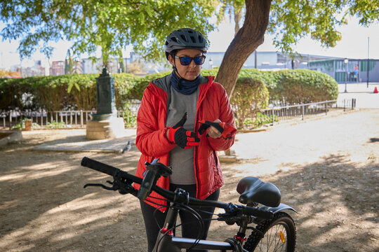 Woman preparing for a bike ride by putting on protective cycling gloves in a park.