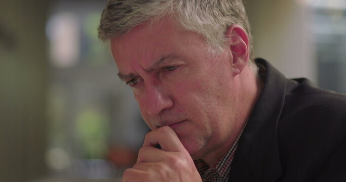 Close-up of middle aged man resting chin on hand in office lounge, deep in thought and focused on decision making in quiet professional setting
