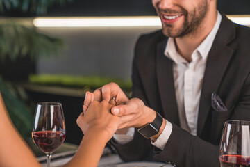 Cropped image of man putting engagement ring on woman's finger during romantic dinner. Valentine`s Day, romantic relationship. Proposal and she said yes