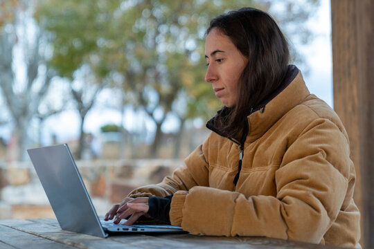 Young woman working on laptop outdoors during autumn, focusing on remote work and digital nomad lifestyle