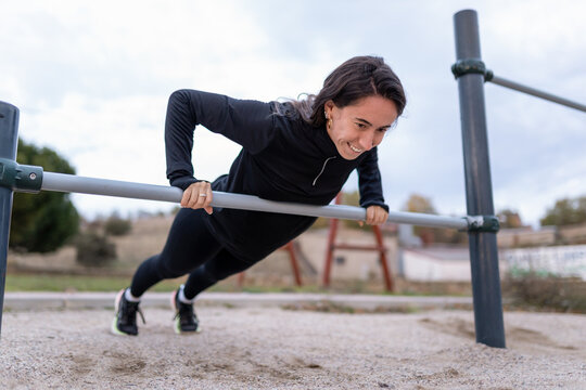 Young woman finding strength and happiness with outdoor calisthenics training on parallel bars