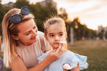 Mother taking care of her daughter while eating ice cream in a park during sunset