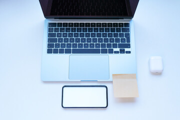 Open laptop with keyboard, smartphone, sticky note and earbuds on white desk; neat study and remote work scene for back to school, productivity and everyday tech lifestyle visuals.