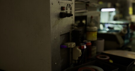 Various factory equipment stands dimly lit, showcasing complex machinery and tools essential for manufacturing. Shadows highlight the industrial atmosphere and organized chaos.