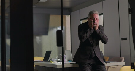 Corporate executive overwhelmed with emotion, covering face with hands during solitary moment in...