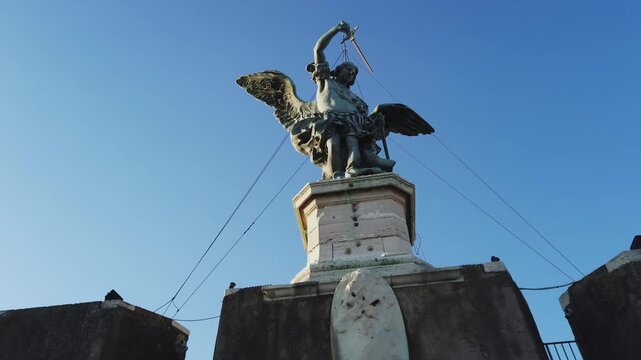 Cinematic shot of beautiful ancient bronze statue of Michael the Archangel, standing on top of the Castle of the Holy Angel, Castel Sant'Angelo in Rome, Italy on sunny day with blue sky