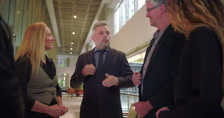 Corporate manager addressing diverse team in office hallway, leading professional conversation with open gestures in bright modern workplace