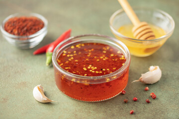 Hot honey in bowl and  chili peppers on green background.