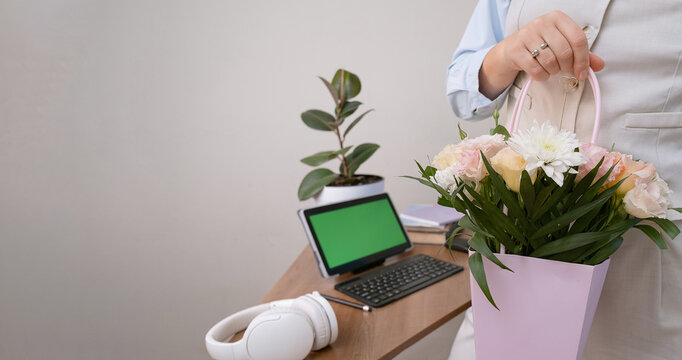 Elegant office woman in a beige suit with a celebratory bouquet for International Women's Day. Clean desk layout with tablet displaying green screen for content replacement. - Powered by Adobe