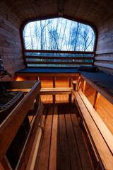 Empty wood fired sauna in a barrel cabin faces a rounded window of leafless trees, early evening...
