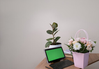 Office workspace featuring a tablet with green screen, keyboard, mouse, and a colorful birthday bouquet, ideal for celebration mockups