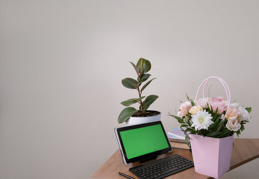 Office workspace featuring a tablet with green screen, keyboard, mouse, and a colorful birthday bouquet, ideal for celebration mockups - Powered by Adobe