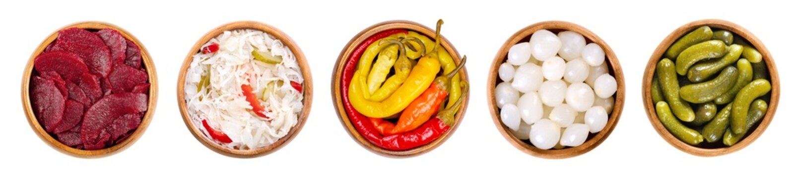 Pickled vegetables in wooden bowls. From left to right beetroot slices, puszta coleslaw, peperoni peppers, pearl onions, and crunchy gherkins, conserved in a vinegar brine with herbs and spices.