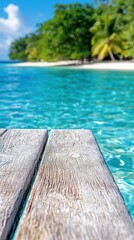 Fototapeta premium Close-up of weathered wooden planks of a pier extending over crystal clear turquoise ocean water. In the background, a white sand beach meets lush green tropica