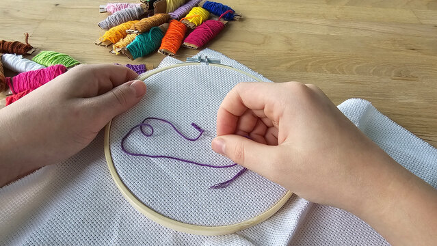 Hands engaged in embroidery with colorful thread in a crafting space concept