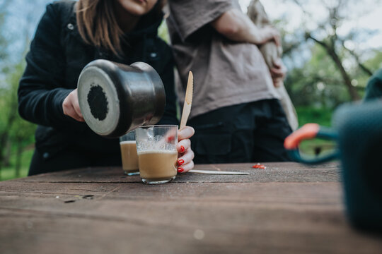 A casual outdoor scene shows people enjoying coffee together. A pouring pot and glass capture a moment of friendship and relaxation in a green park setting. - Powered by Adobe
