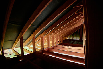 Wooden roof framework showing unfinished attic space with exposed beams and rafters, sunlight...