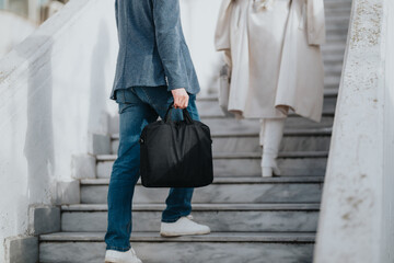 A casual business scene on stairs shows a person in jeans and blazer carrying a black bag, while another in a light coat follows, symbolizing work, commuting and everyday professional life.