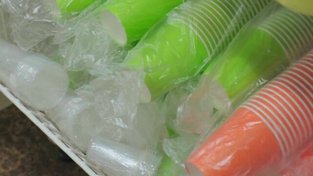 A close-up of various paper and plastic cups, colorful party supplies, and disposable tableware displayed on a grocery store shelf. Clutter, waste, environmental problems. Recycle plastic