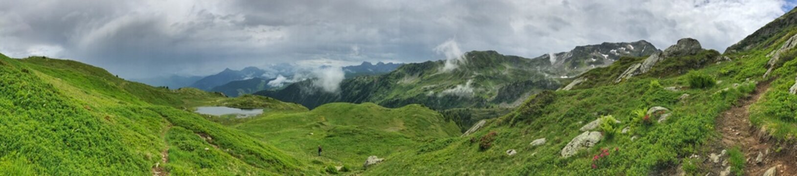 Panoramic view of lush green alpine landscape with mountains and cloudy sky