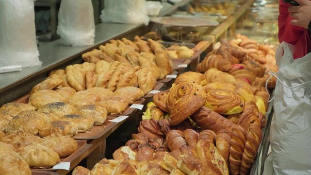 Variety of freshly baked pastries, croissants, sweet rolls arranged in bakery or cafe display window. Grocery store setting, highlighting artisanal bread and inviting breakfast, brunch and dessert