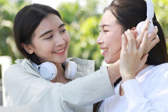 Pretty cheerful asian woman in casual clothes browses laptop computer connected to 4g internet updates software uses modern technologies poses outdoor looks gladfully away with her friend.