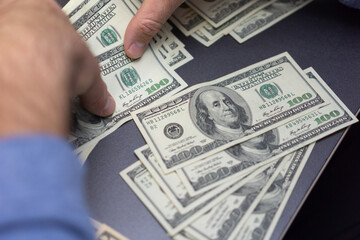 Close-up view of hands sorting multiple 100 bills on a dark desk, illustrating money handling, finance tasks, budgeting, and cash operations.