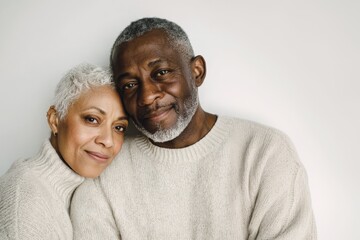 Portrait of a cute mature African American couple wearing beige sweater looking to camera over white wall.