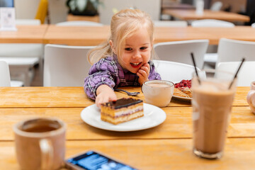 Little child girl eats cakes and pastries in a cafe