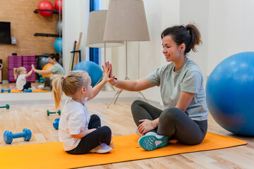 Mother and daughter child sit on the mat and high-five each other in the gym