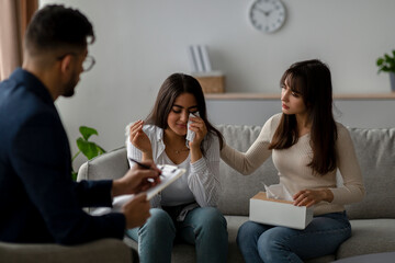 In a counseling session, a young Arab woman is crying while her partner comforts her. They are discussing their relationship issues with a counselor in a warm, supportive environment.