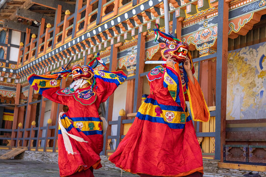 Jakar, Bhutan - 24 September 2025: View of vibrant dancers in ornate red and gold costumes, their masks a kaleidoscope of color against the backdrop of traditional Bhutanese architecture.
