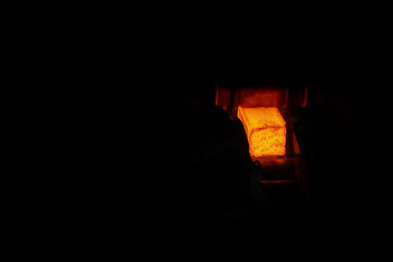 Red-hot metal bar being heated inside an industrial furnace during a steel or metalworking process. The glowing material shows the intensity of the high-temperature environment.