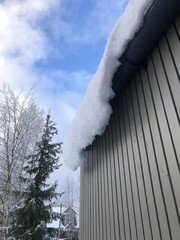 White snow slides down from the roof like a white avalanche, winter landscape, low angle