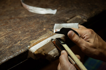 Violin making by hand bow. Close-up of an artisan&rsquo;s hands sanding or shaping a tool handle on a workbench. 