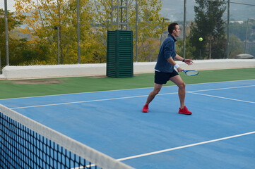 Obraz premium Active Man Playing Tennis On Outdoor Blue Court With Green Surroundings