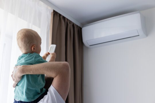 Little child sitting on fathers shoulders trying to switch on air conditioner with remote control.