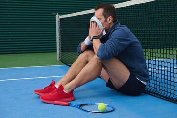 Tired Tennis Player Resting Against Court Net After Match Frustration and Fatigue