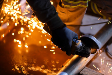 Close-up of a worker using an angle grinder on metal, producing bright sparks. The image illustrates industrial manufacturing and metalworking processes.