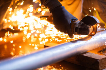 Close-up of a worker using an angle grinder on metal, producing bright sparks. The image illustrates industrial manufacturing and metalworking processes.