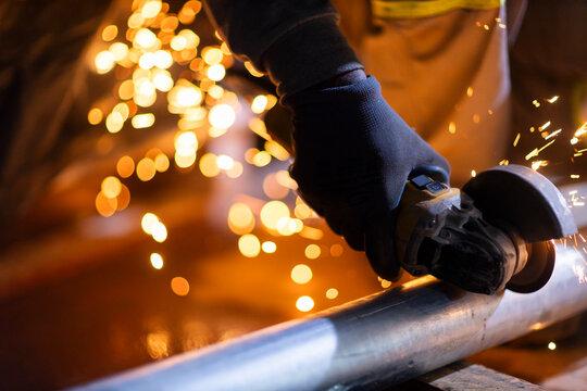 Close-up of a worker using an angle grinder on metal, producing bright sparks. The image illustrates industrial manufacturing and metalworking processes. - Powered by Adobe