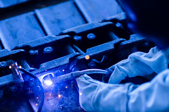 Close-up of a worker using an angle grinder on metal, producing bright sparks. The image illustrates industrial manufacturing and metalworking processes.